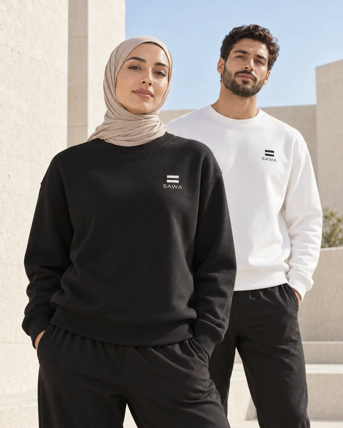 Une femme sportive en foulard beige et pull noir SAWA, avec un homme en pull blanc à l’arrière-plan
